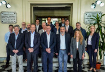 Delegación de la UE visitó el Teatro Larrañaga en Salto Group of EU delegation members in suits posing on steps in a historic theater lobby; accompanying news banner below about the visit to Teatro Larrañaga in Salto.