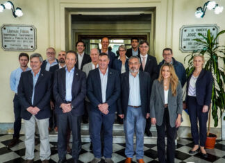 Delegación de la UE visitó el Teatro Larrañaga en Salto Group of EU delegation members in suits posing on steps in a historic theater lobby; accompanying news banner below about the visit to Teatro Larrañaga in Salto.