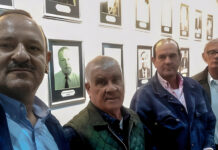 Reclaman ambulancia y mejoras urgentes en caminos rurales de Saucedo: vecinos denuncian aislamiento sanitario Group of men standing in a gallery with framed photos on the wall; a news banner at the bottom reports 'Reclaman ambulancia y caminos rurales en Saucedo'.