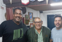 Bien por ellos Group of three smiling men posing for a photo in a room with plaques on the wall; a green sports banner at the bottom reads 'Deportes' and 'Bien por ellos' with additional article text.