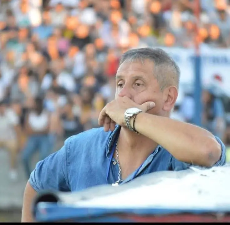 Man in a blue denim shirt rests his chin on his hand, watching a crowded outdoor event.
